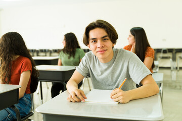 Confident high school student taking notes in classroom with other students learning