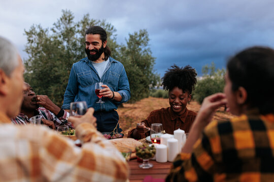 Friends enjoying outdoor dinner party with wine in olive grove