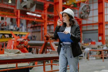 Woman engineer manager standing at steel production factory. Female inspector wears safety hard hat...