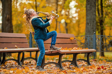 Young girl playing saxophone in autumn park. Child musician practicing instrument outdoors on a...