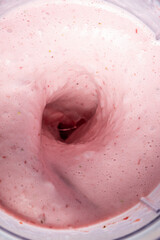 The process of making a strawberry milkshake, whisking all the ingredients in a blender.