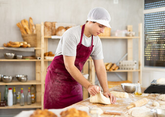 Guy baker in uniform prepares raw dough, kneads it with his hands