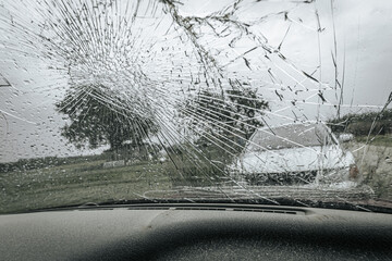 A cracked car windshield seen from the inside, with raindrops and a blurred outdoor scene including...