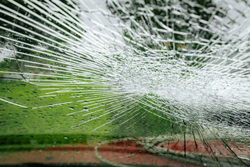 A cracked car windshield seen from the inside, with raindrops and a blurred outdoor scene including...