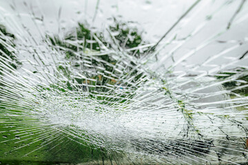 A cracked car windshield seen from the inside, with raindrops and a blurred outdoor scene including...