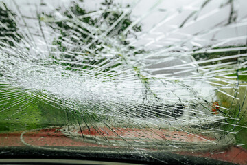 A cracked car windshield seen from the inside, with raindrops and a blurred outdoor scene including...
