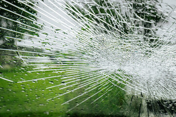 A cracked car windshield seen from the inside, with raindrops and a blurred outdoor scene including...