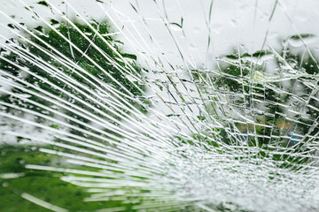A cracked car windshield seen from the inside, with raindrops and a blurred outdoor scene including...