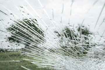 A cracked car windshield seen from the inside, with raindrops and a blurred outdoor scene including...
