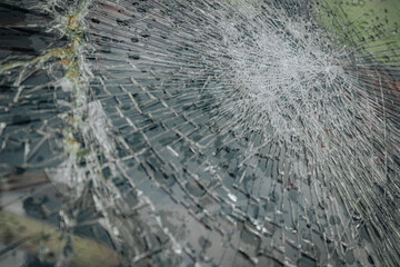 A cracked car windshield seen from the inside, with raindrops and a blurred outdoor scene including...
