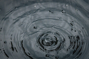 A water droplet creates a splash and a crown-like spike on a calm dark surface, captured in a...