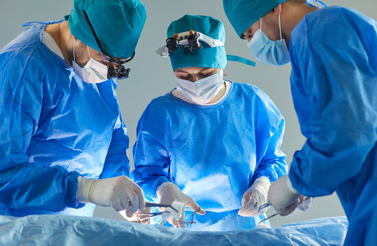 Team of professional doctors surgeons wearing blue medical uniform performing surgical operation in modern operating room at hospital. Medicine, surgery and emergency help concept.