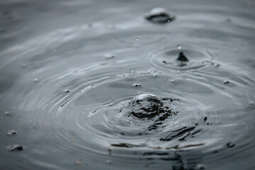 A water droplet creates a splash and a crown-like spike on a calm dark surface, captured in a...