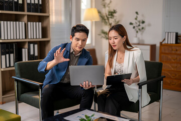 Two people are sitting on chairs in a room, looking at a laptop