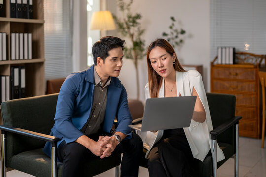 A man and a woman are sitting on a couch, looking at a laptop