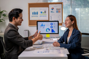 A man and a woman are sitting at a desk with a computer monitor in front of them