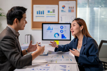 Two people are talking in a room with a lot of graphs on the wall