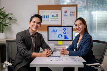 Two people are sitting at a desk with a computer monitor in front of them