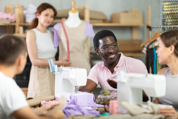 Friendly middle-aged man talking with woman and sewing, other working with mannequin in dressmaking courses