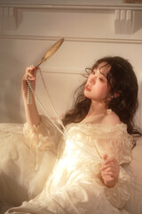 Young woman in soft light with pearls and hand mirror.