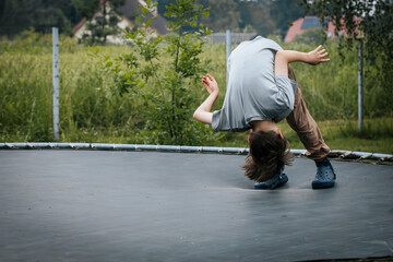 Boy mid-backflip on a trampoline in a garden setting, wearing casual clothes and Crocs, showcasing...