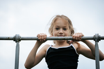 A girl in mid-air performs an acrobatic flip outdoors against a cloudy sky, captured in motion with her body arched and arms extended, conveying energy and freedom.