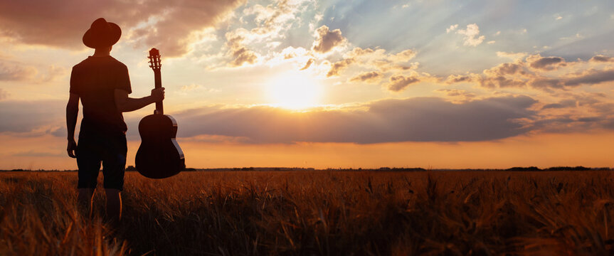 silhouette of man holding guitar standing in sunset field, music festival banner, musician with copyspace