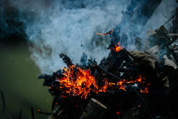 Close-up of burning logs and dry leaves with vivid flames and smoke rising, capturing the intense...