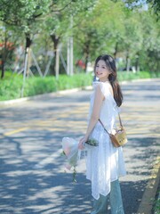 Smiling young woman in a white dress on a sunny street.