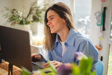 Beautiful young  woman working using computer laptop concentrated and smiling, she sitting at home, freelancer, girl have video call conference. Woman wear blue shirt, look happy.