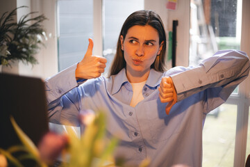 Young brunette woman freelancer using computer laptop at home doing thumbs up and down, disagreement and agreement expression. crazy conflict, like or not.