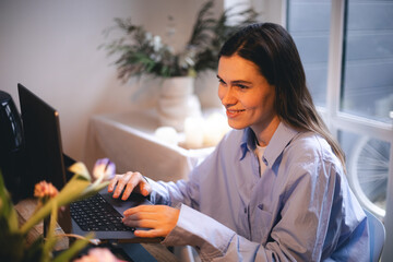 Smiling young woman sit at desk work on laptop or watching webinar, happy girl feel excited browsing internet on computer, using wireless home connection. Technology concept, girl wear blue shirt.