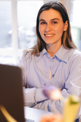 Smiling young woman sit at desk work on laptop or watching webinar, happy girl feel excited browsing internet on computer, using wireless home connection. Technology concept, girl wear blue shirt.