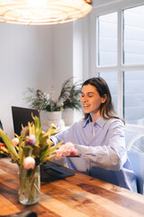 Smiling young woman sit at desk work on laptop or watching webinar, happy girl feel excited browsing internet on computer, using wireless home connection. Technology concept, girl wear blue shirt.