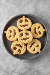 Halloween pumpkin shaped sandwich cookies with sweet cream filling on a gray plate with milk on a concrete background. Jack o lantern cookies. Top view.