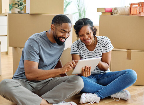 Portrait of a young couple unpacking, moving in and relocation to a new apartment, happy young couple using a tablet, browsing and shopping online, , family new beginning sitting on the floor