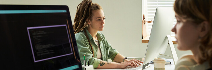 Young adult Caucasian woman with dreadlocks developing neural network on computer, sitting at desk...