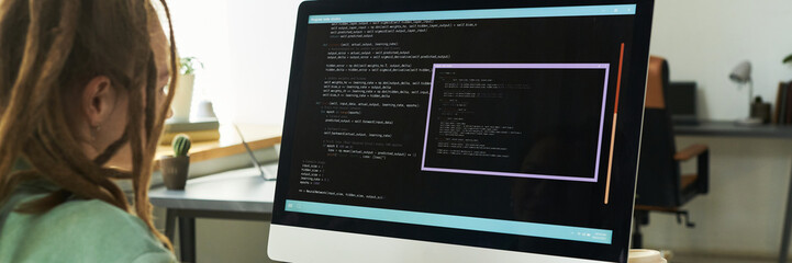 Teenage Caucasian girl sitting at desk working on neural network development coding on large...