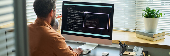 Caucasian middle aged man sitting at desk developing neural network code on large desktop computer...