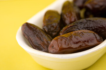 Freshly harvested dates served in a white bowl on a bright yellow background