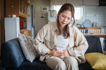 	自宅でお腹を痛めて苦しそうな女性

A woman suffering from stomach pain at home