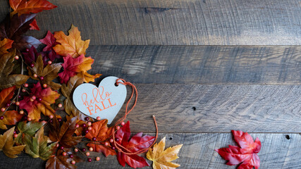 Hello Fall heart shaped tag with colorful autumn foliage banner on a dark walnut, wooden background