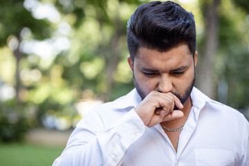 Unwell South Asian young adult man suffering from cold or flu with allergic runny nose, nasal viral...