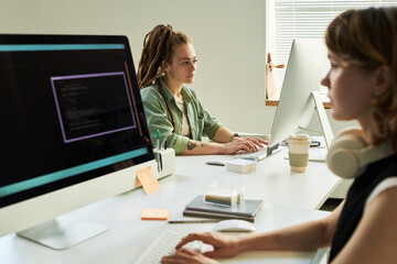 Woman developing neural network while sitting at desk next to young adult Caucasian woman working...