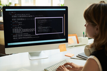 Caucasian young adult woman developing neural network code on desktop computer, sitting at desk,...