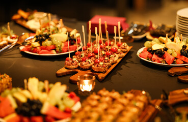 Elegant appetizer platter with bite-sized tarts and cherry tomatoes on skewers, surrounded by fresh fruit arrangements. Warm candlelight enhances the festive mood.