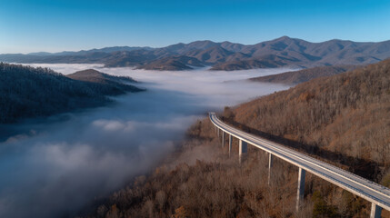 Obraz premium breathtaking aerial view of mountains shrouded in morning fog with delicate bridge spanning deep valley