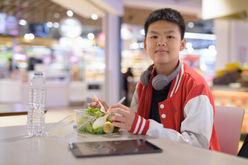 Teen Thai boy wearing headphones eating salad in cafeteria © Ranta Images