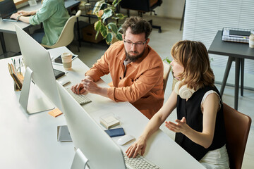 Caucasian middle aged man and Caucasian young adult woman collaborating at workstation, discussing...