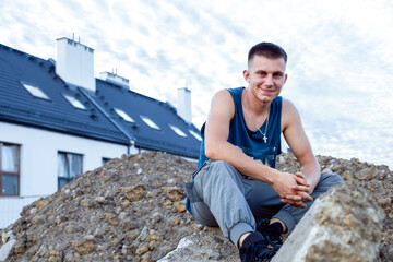 young man sitting on the rocks,  Young handyman posing on a pile of earth against the backdrop of...